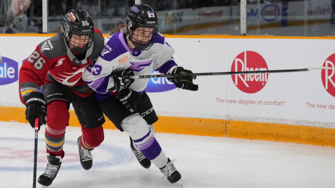 Two female hockey players competing on the ice, one in a red jersey and the other in a white and purple jersey, with a focus on their intense gameplay and teamwork.